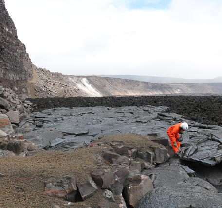 Color photograph of scientist collecting lava sample from crater floor