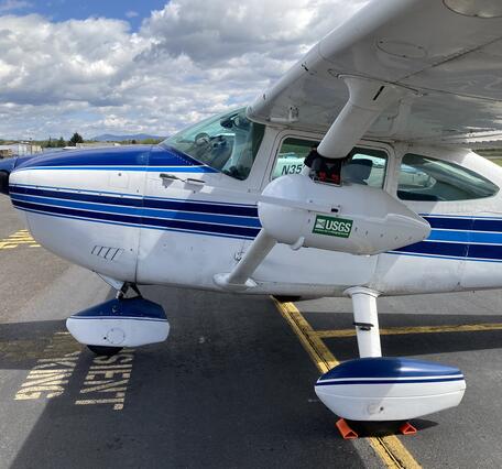 a small white aircraft with a blue, white, and black stripes running down the middle and plane nose.
