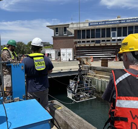 People on a dock lowering a big piece of equipment into the water