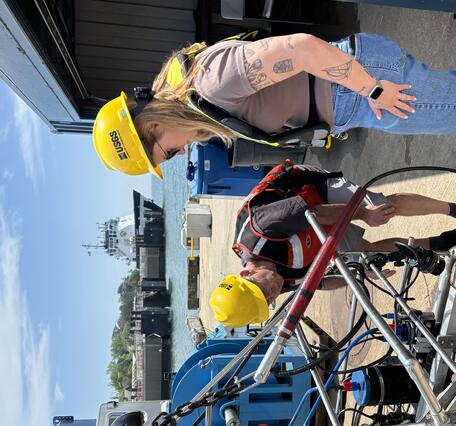 Two people inspecting a big piece of equipment on a dock outside