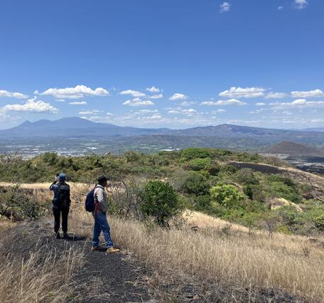Color photograph of two people overlooking a volcanic landscape on a sunny day