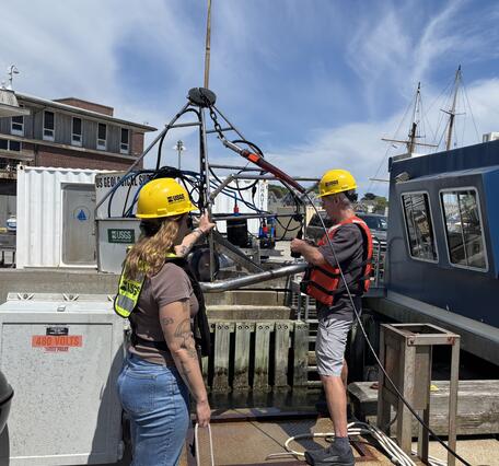 Two people working with large equipment on a dock
