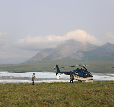 two people near helicopter with mountains in the background