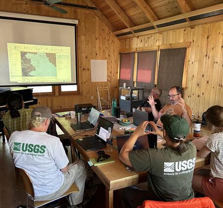A group of seven researchers sits around a table in a wood-paneled room
