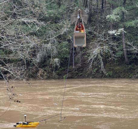 man pulls cable car across rushing brown water with a yellow pontoon in tow that has sensors recording the flow