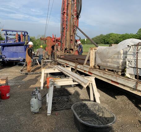 USGS staff in hard hats work at a drill rig. 