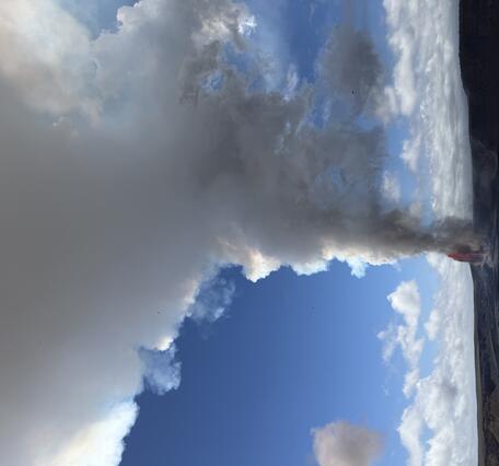 Large white plume of volcanic gas and steam rising from lava fountains in a crater