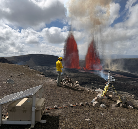 Two lava fountains erupt from vents on crater floor as scientist monitors in the foreground