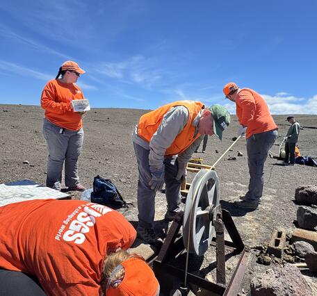 Several scientists working around a hole in the ground that is a well