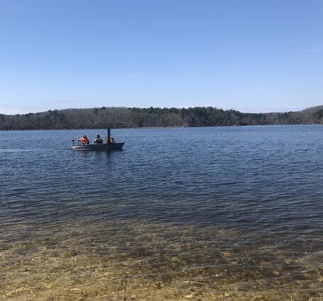 small boat on pond, trees lining the edge of the pond