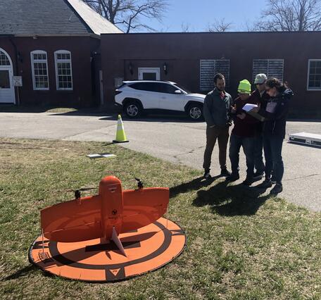 four people standing together looking at screen outside with drone on the ground
