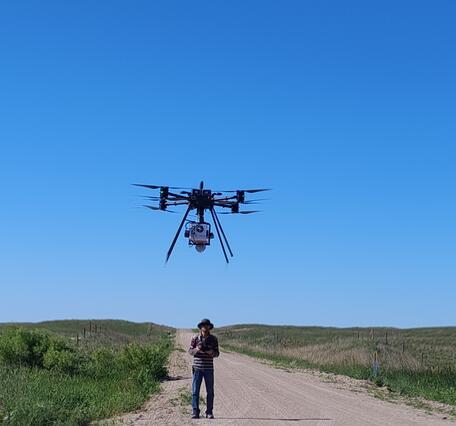 A person operates a drone in a grassland prairie