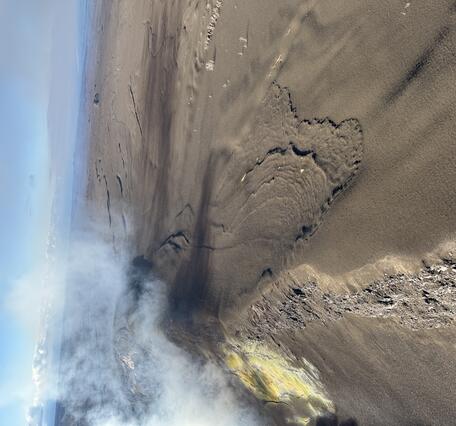 Color photograph showing volcanic gas wafting over a tephra-blanketed crater rim