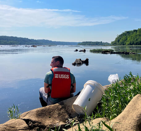 A hydrologic technician sits at the edge of a river.