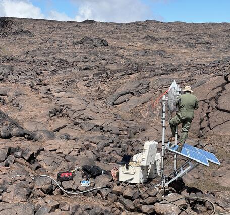 Color photograph of field engineer working on remote volcano monitoring station located on a lava flow