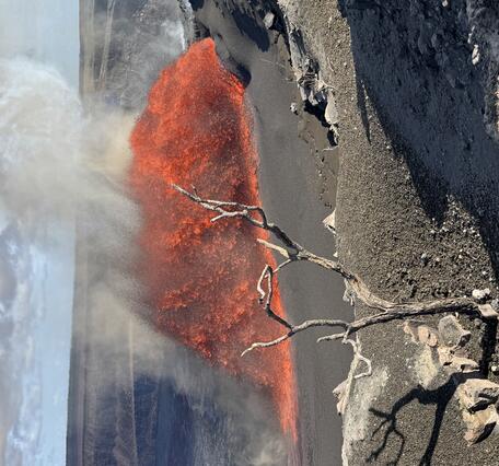Color photograph of lava fountain with dead tree in foreground