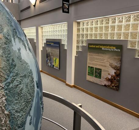 A portion of a large globe with scientific displays on a wall in the background