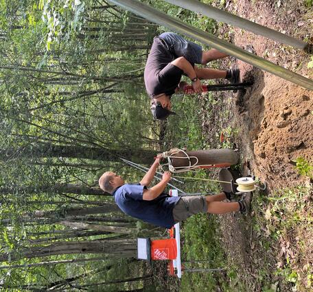 Two men install a groundwater well in the woods.