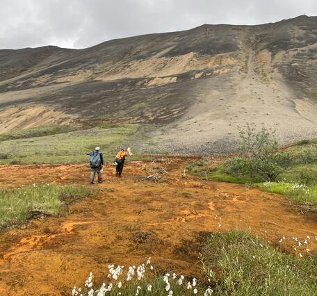 Two people walking across and orange seep.