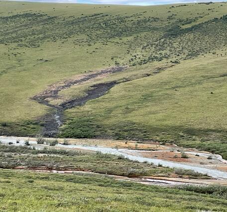 A blue creek running down a hillside into an orange river.