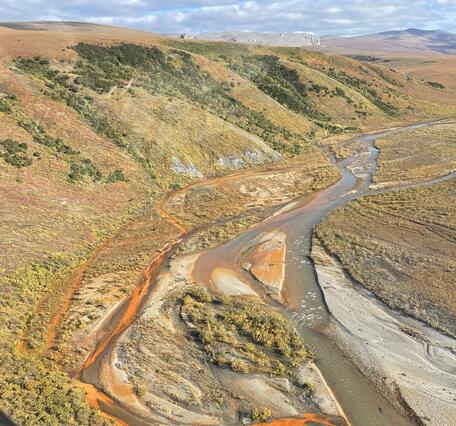 An orange stream flowing into a larger blue river.