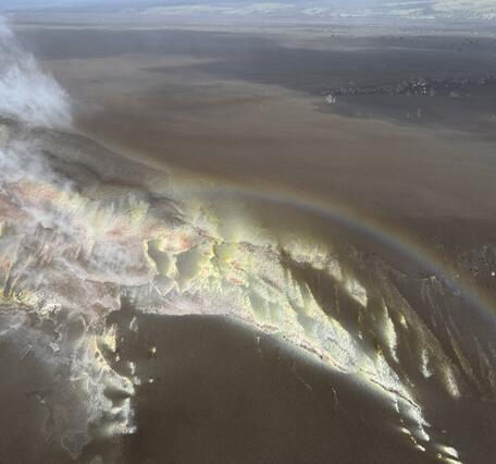 Color photograph of sulfur deposits on crater rim, with rainbow