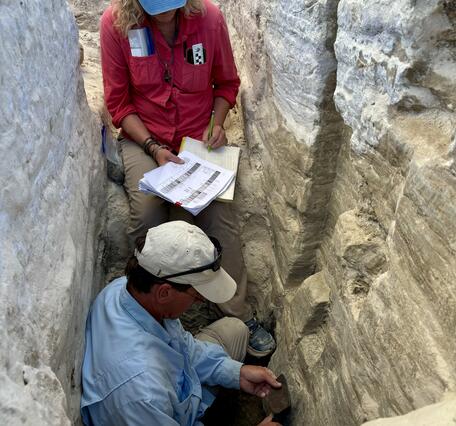 Two people examine sediment layers in a trench