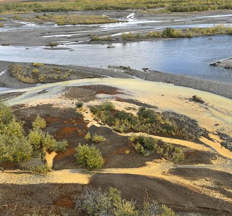 Pale orange creek flowing into clear blue river.