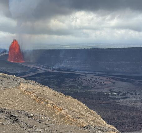 Color photograph of lava fountain with crater rim in foreground