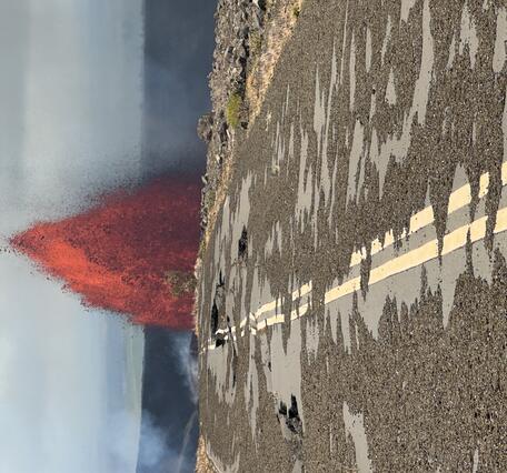 Color photograph of lava fountain with broken road in foreground
