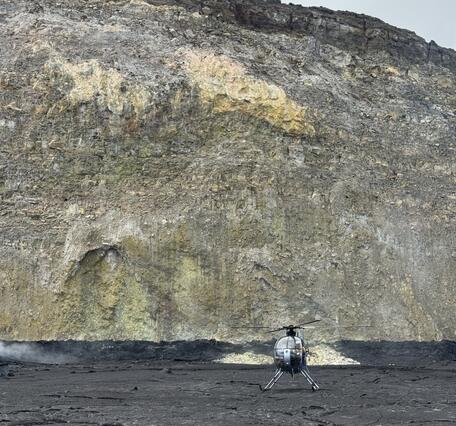 Color photograph of helicopter on crater floor with crater wall in background