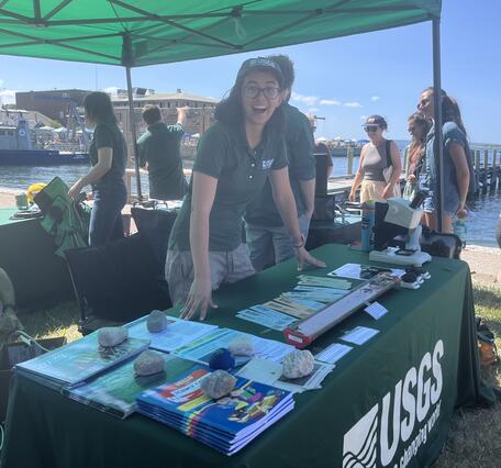person standing behind USGS booth outside under tent