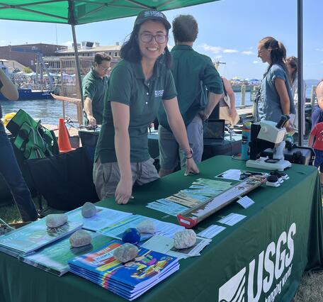 person standing behind USGS booth outside under tent