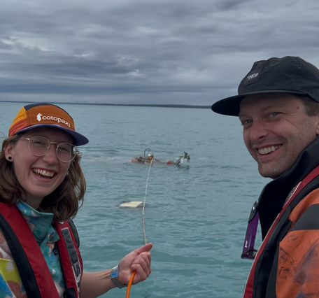two people smiling, equipment in the water behind them