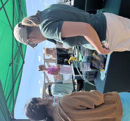 USGS scientist talking to two young adults at USGS booth outside under a tent