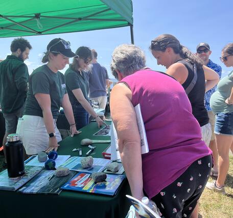 People in USGS shirts behind booth outside under tent talking to visitors