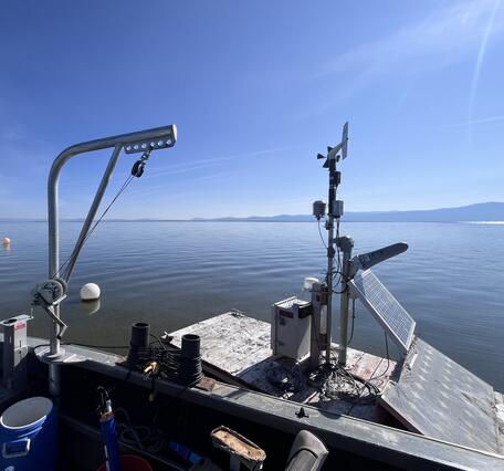 boat with equipment pulls up to floating platform housing water-quality instruments on a bright blue summer day