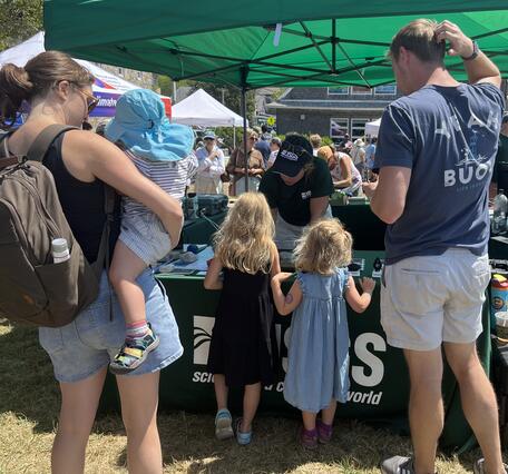 a family with three kids visiting the USGS booth outside under a green tent