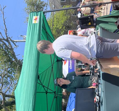 USGS scientist at booth outside with drones on it under tent outside talking to a person