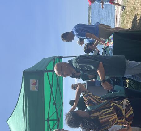 Two people talking to USGS scientist next to USGS booth outside under green tent on a sunny day