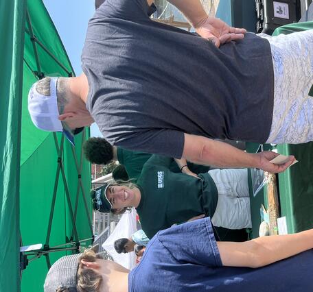 woman smiling, talking to a man and kid, outside at USGS booth