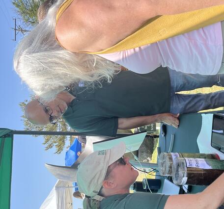 USGS scientist showing visitor something on a tablet on a table outside under a tent