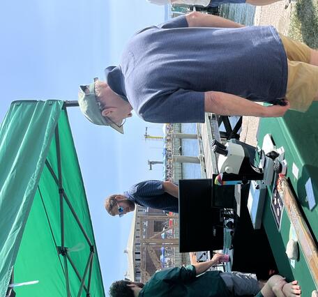 Person sitting at USGS booth under tent outside, smiling at person visiting the booth