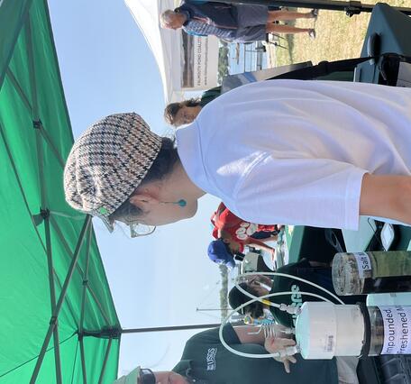 Person in USGS shirt at booth under tent outside talking to person while referencing equipment on the table