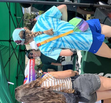 people visiting USGS booth outside under tent on a sunny day