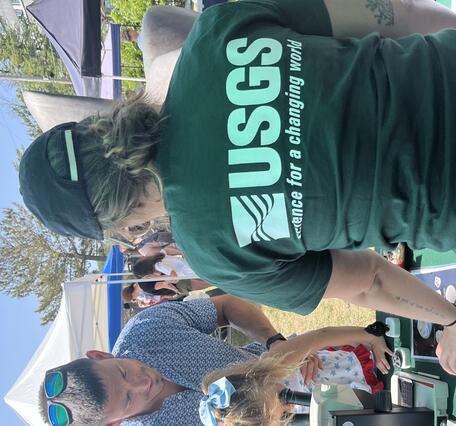 Father holding daughter up to look through microscope, while USGS 