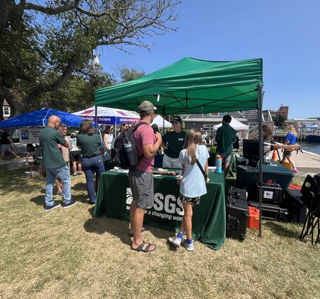 USGS booth under tent outside by the ocean, people talking to USGS at the booth