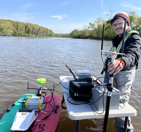 A hydrologic technician poses with an autonomous miniature boat in the Anacostia River.