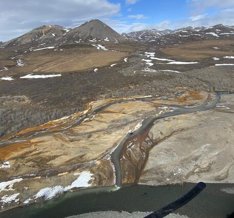 Orange river on a brown landscape and snowy mountains in the background.