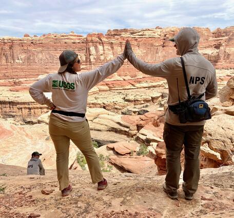 A USGS and NPS scientist give each other a high-five while doing fieldwork